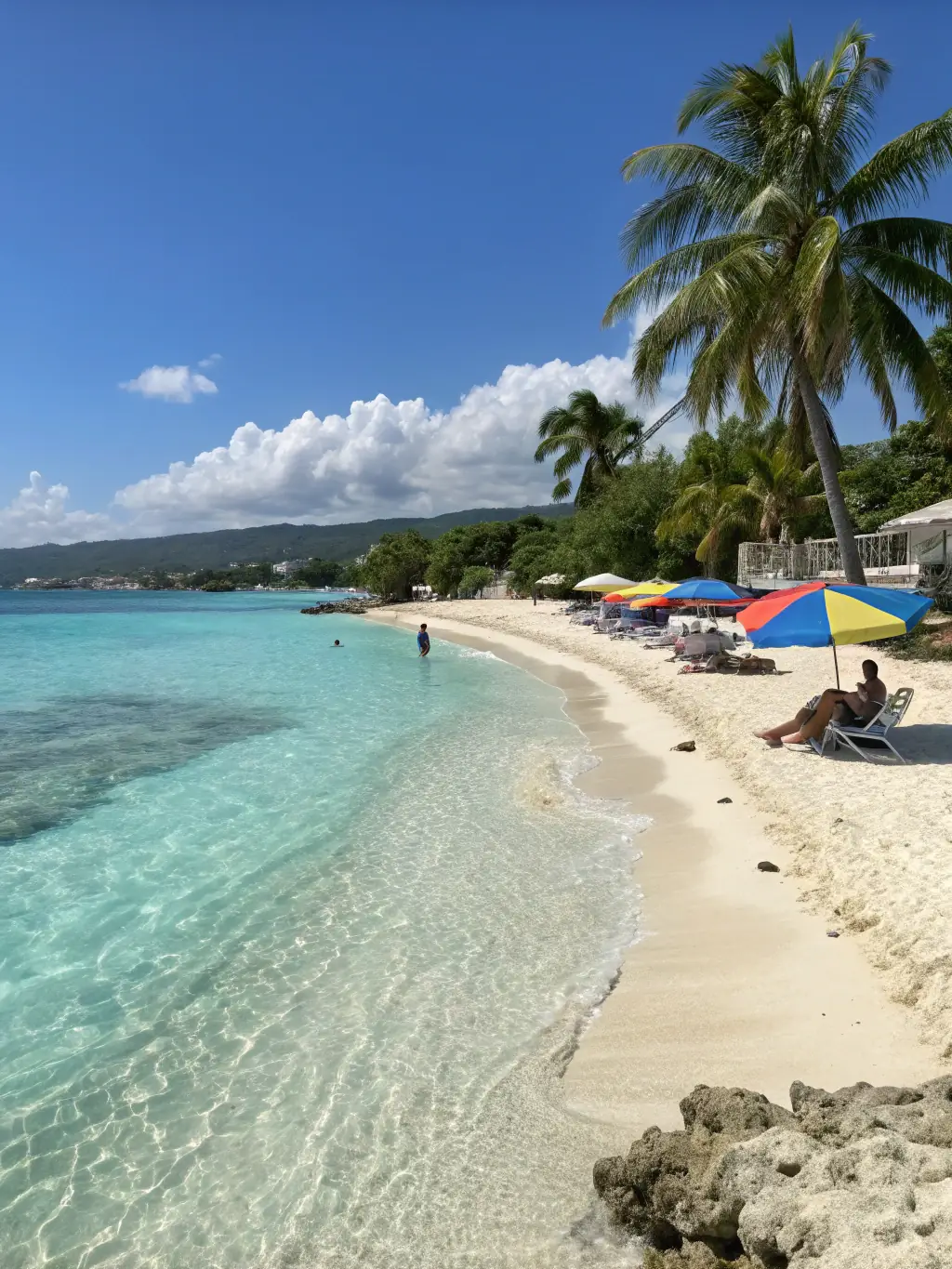A serene image of Doctor's Cave Beach in Montego Bay, Jamaica, showcasing crystal-clear turquoise waters and white sand, with a few people relaxing under umbrellas.